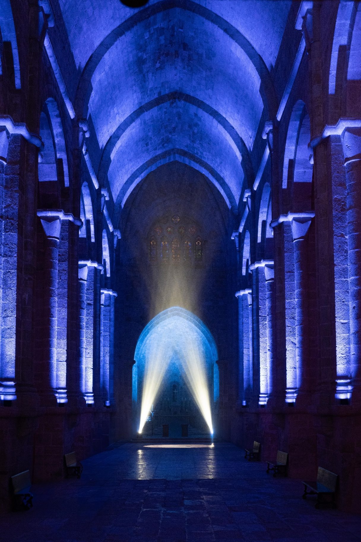 Gothic nave lit in blue with two white light beams converging to the floor, Fontfroide Abbey.